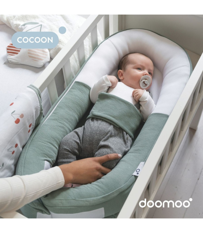 Bebé dentro del reductor Doomoo Cocoon Tetra Green verde colocado en la cuna, con un adulto al lado
