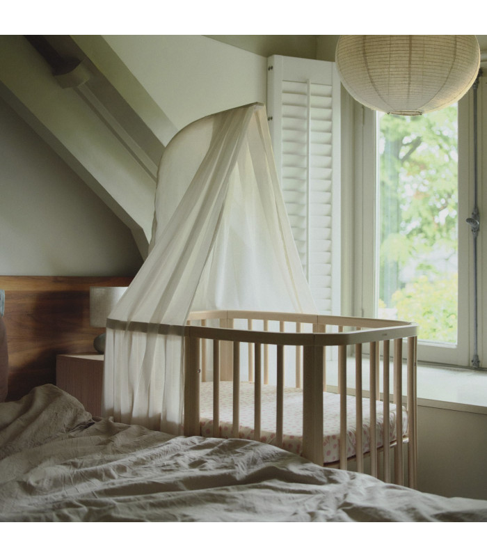 Stokke Nighti con dosel blanco colgado del mástil, junto a la ventana