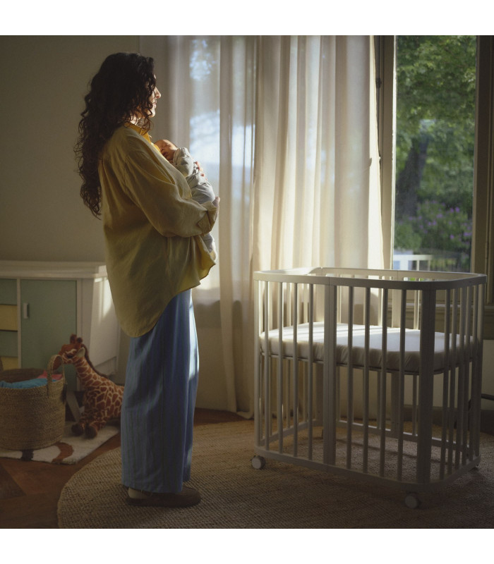 Madre con su bebé junto a la minicuna Stokke Nighti Mini, disponible en Madrid