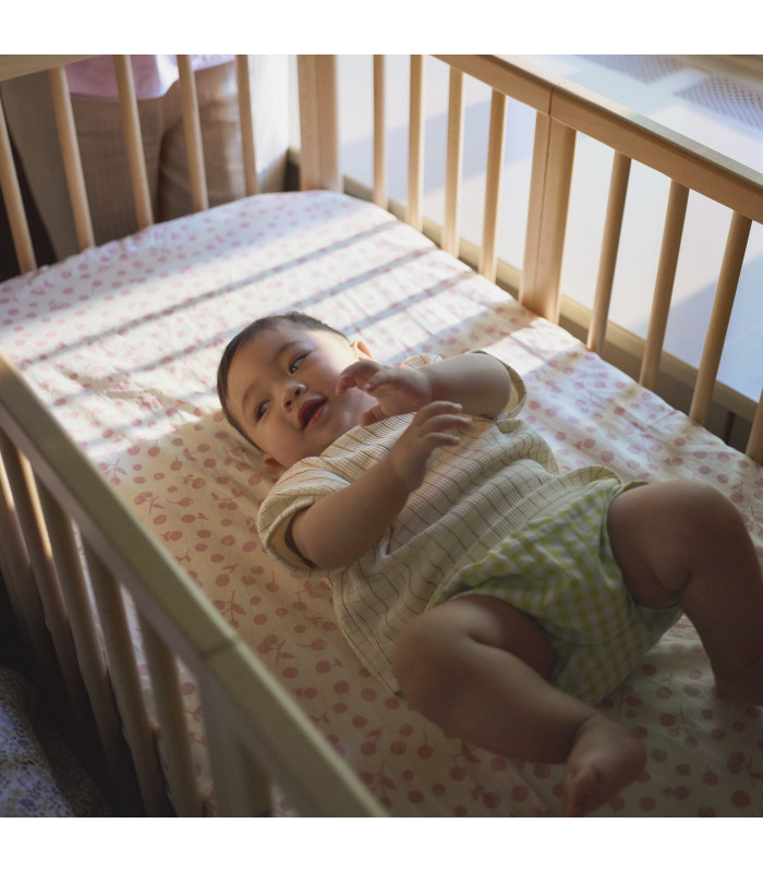 Bebé tumbado sobre una bajera Stokke Wild Rose en la cuna Nighti, disponible en Madrid